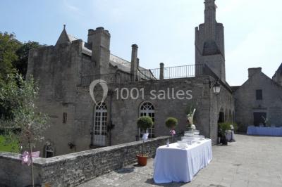 Château en pierre éclairé par des lampadaires au crépuscule, entouré d'arbres et d'une allée gravillonnée.