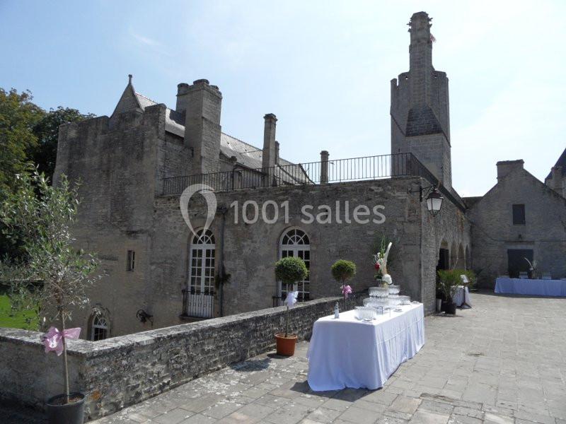 Table décorée pour un événement sur une terrasse en pierre, devant un bâtiment ancien en pierre avec cheminées.