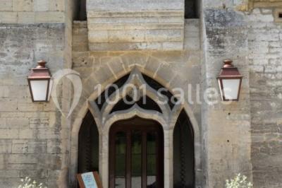 Château en pierre éclairé par des lampadaires au crépuscule, entouré d'arbres et d'une allée gravillonnée.