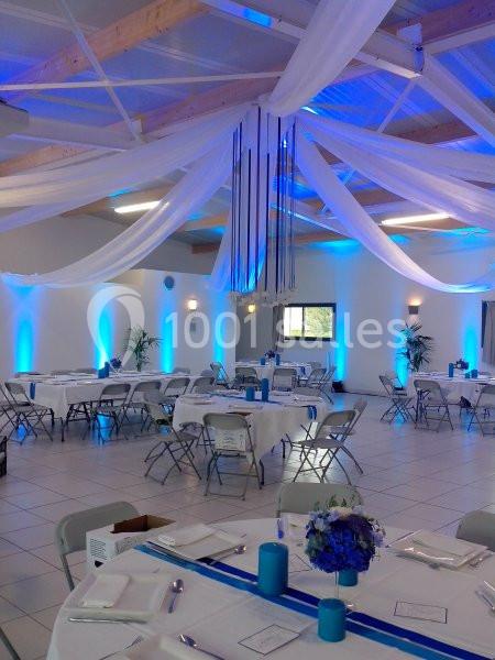 Salle de réception décorée avec des drapés blancs suspendus, éclairage bleu et tables dressées pour un événement.