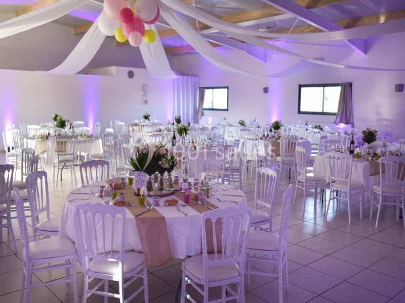 Salle de réception décorée avec des tables rondes, nappes blanches, chaises assorties et guirlandes suspendues.