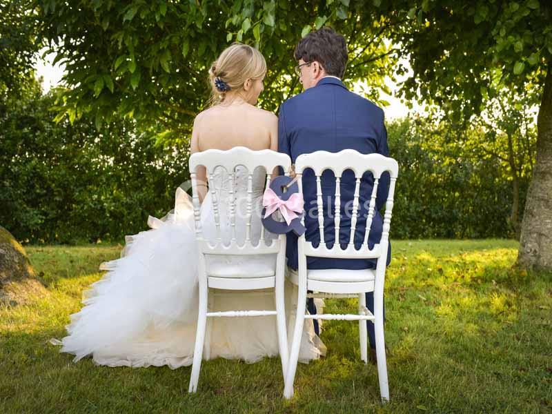 Un couple assis de dos sur des chaises blanches dans un jardin, entouré de verdure.