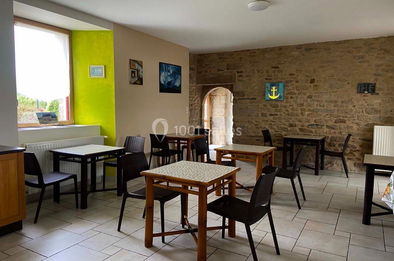 Salle à manger lumineuse avec murs en pierre, tables en bois, chaises noires et une fenêtre donnant sur l'extérieur.