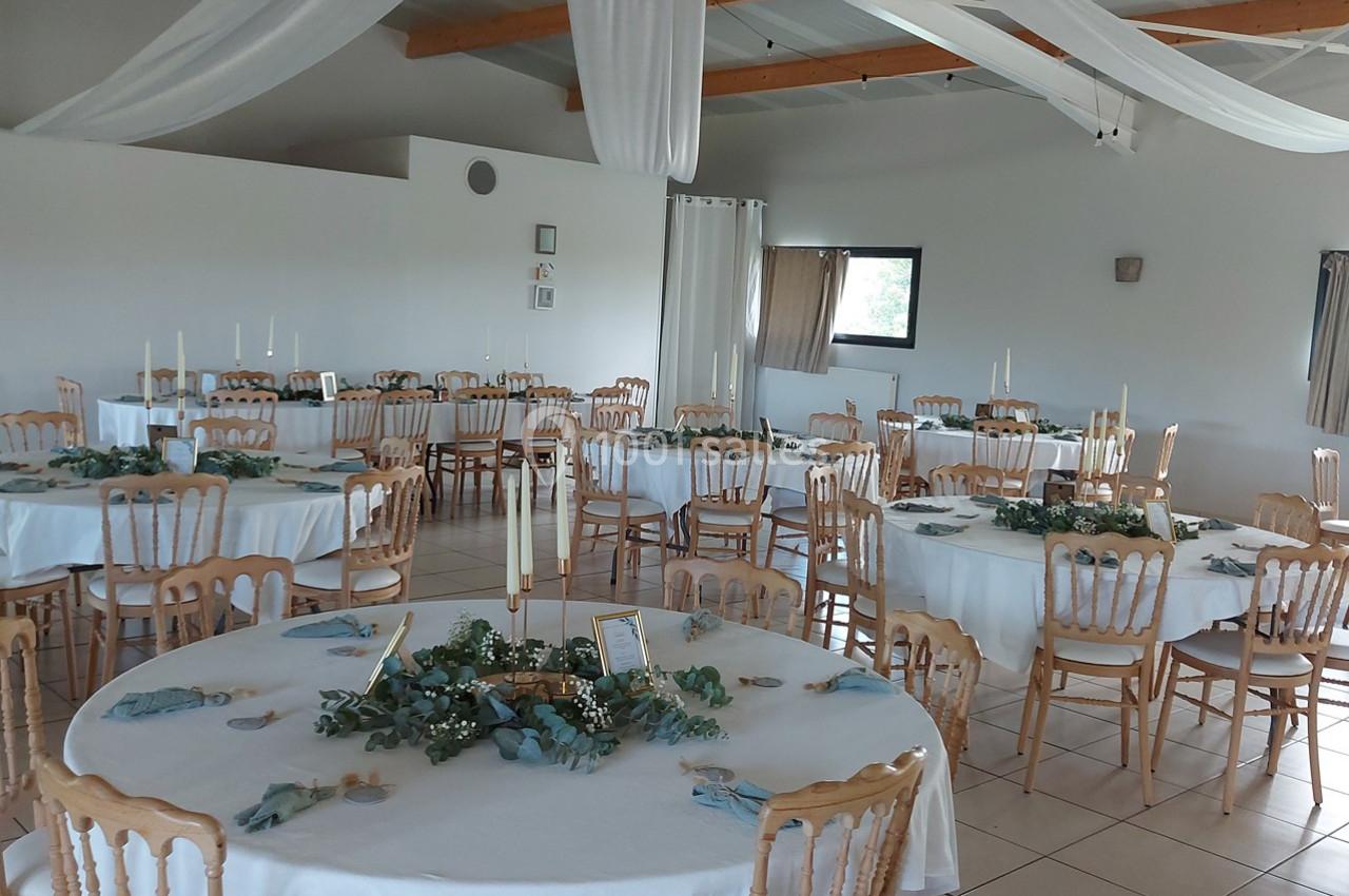 Salle de réception décorée avec des tables rondes, nappes blanches, chaises en bois et centres de table végétaux.