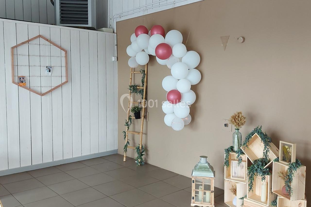 Décoration murale avec arche de ballons blancs et roses, échelle en bois, lanternes et étagères ornées de plantes.