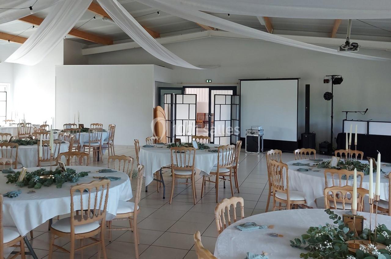 Salle de réception décorée avec des tables rondes, nappes blanches, chaises en bois clair et guirlandes végétales.