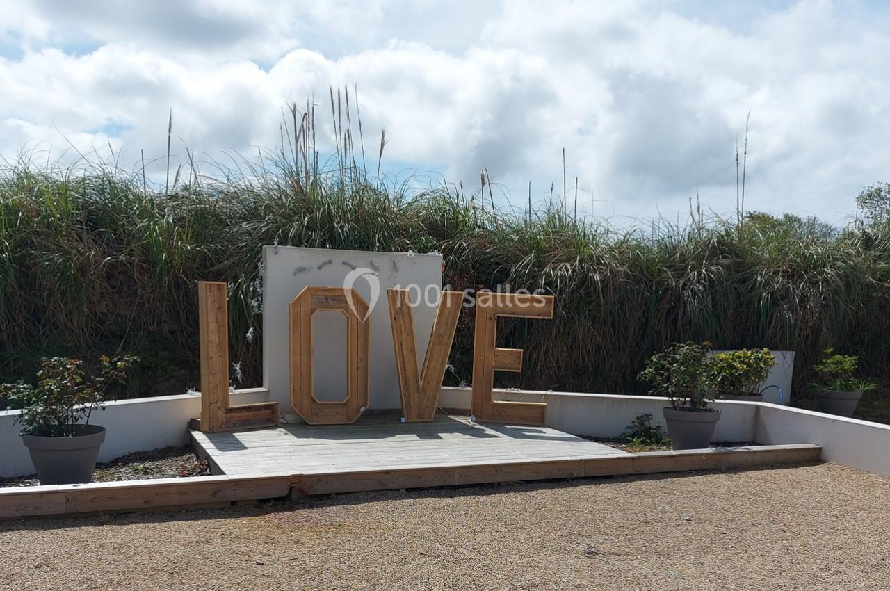 Lettres géantes formant le mot ’LOVE’ en bois, installées sur une plateforme devant des herbes hautes.