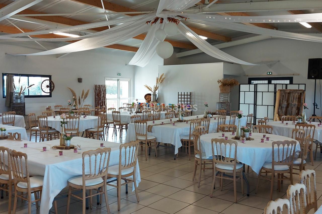 Salle de réception décorée avec des tables rondes dressées, nappes blanches et éléments décoratifs suspendus.