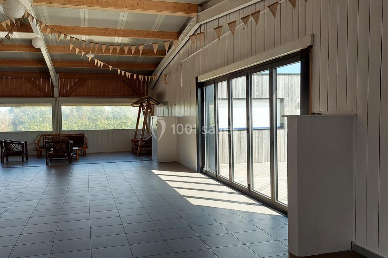 Salle lumineuse avec carrelage gris, grandes baies vitrées, plafond en bois et guirlandes décoratives suspendues.