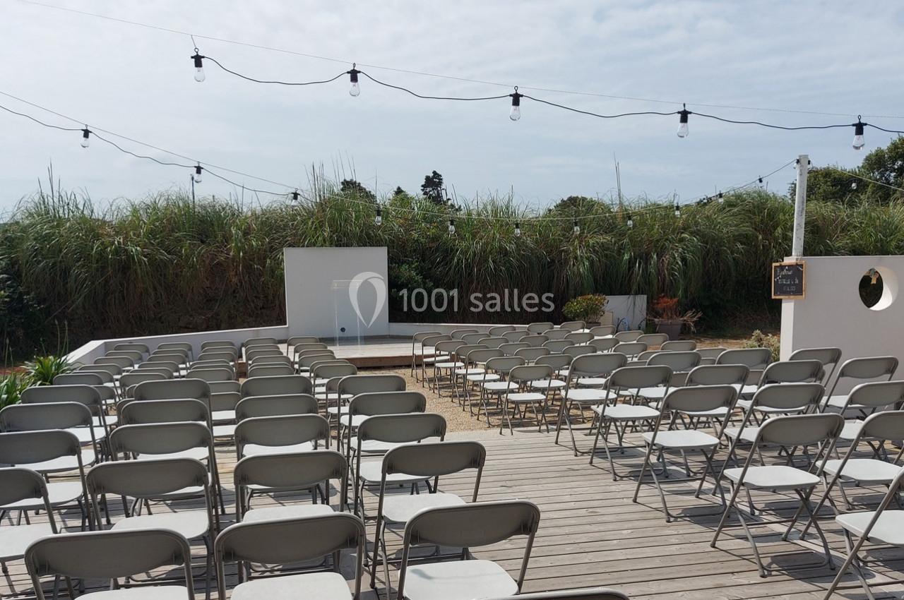 Chaises pliantes alignées sur une terrasse en bois, face à un écran blanc en extérieur, sous des guirlandes lumineuses.
