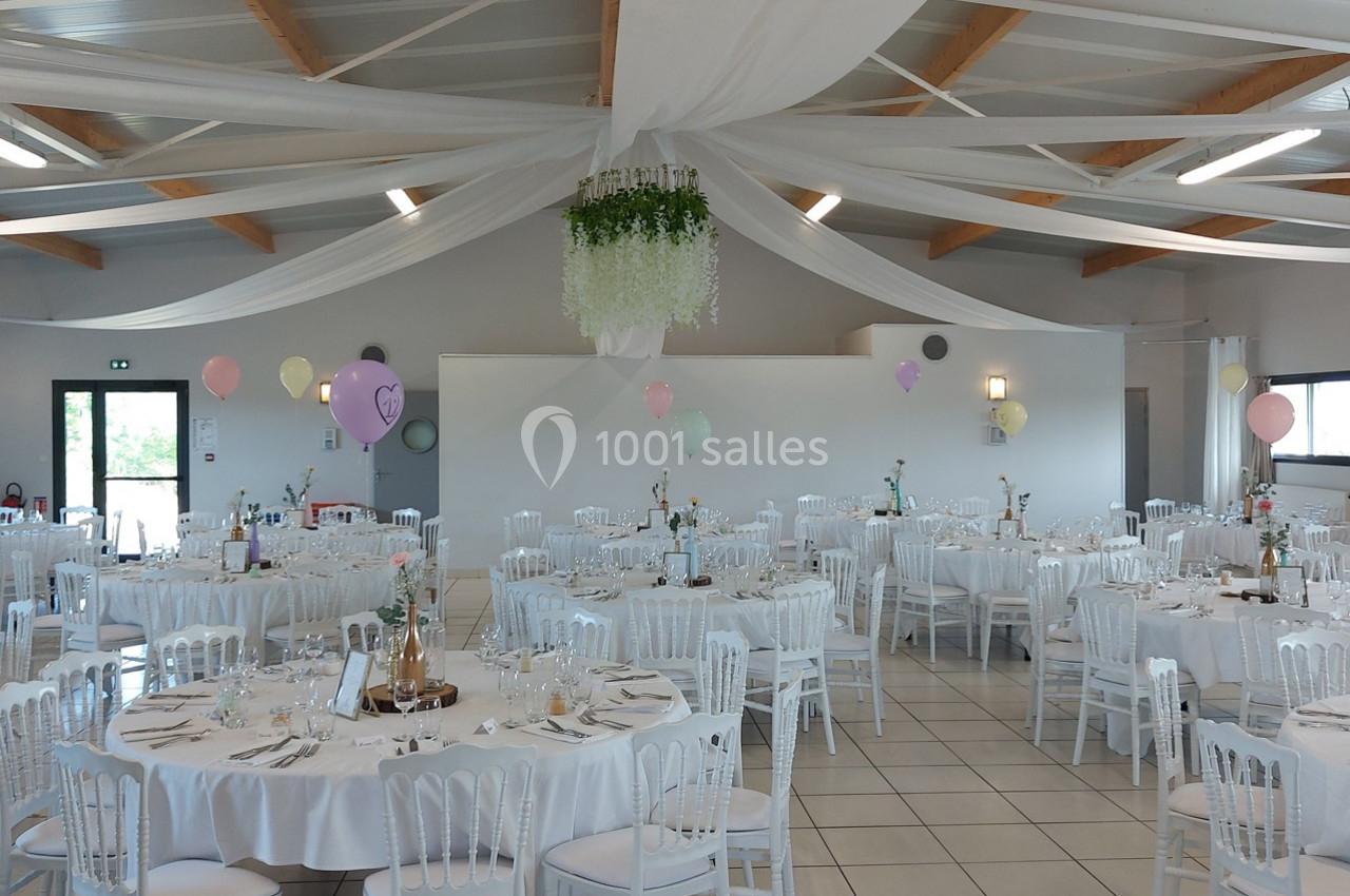 Salle de réception décorée avec des tables rondes, nappes blanches, chaises assorties et ballons colorés suspendus.