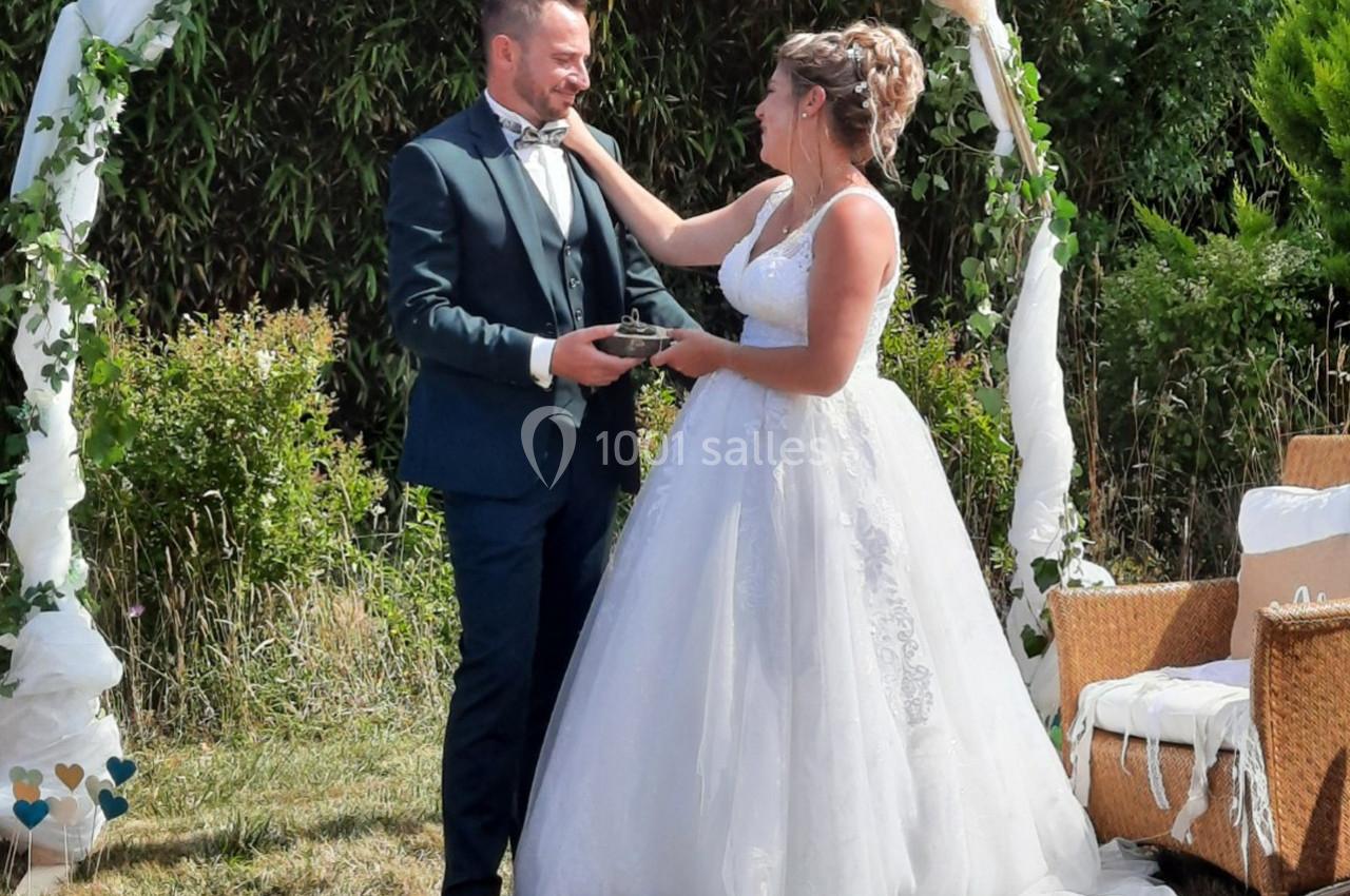 Un couple en tenue de mariage échange un moment tendre sous une arche décorée dans un jardin.