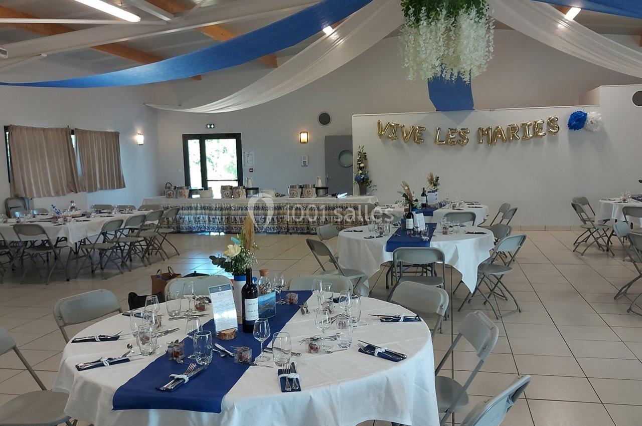 Salle décorée pour un mariage avec tables dressées, nappes blanches, chemins de table bleus et guirlande ’Vive les mariés’.