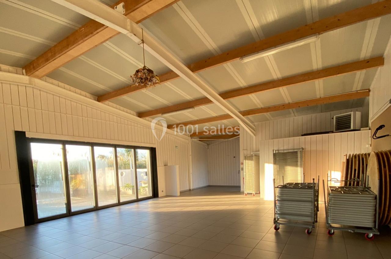 Salle lumineuse avec plafond en bois, grandes baies vitrées, carrelage au sol et chariots de rangement sur roulettes.