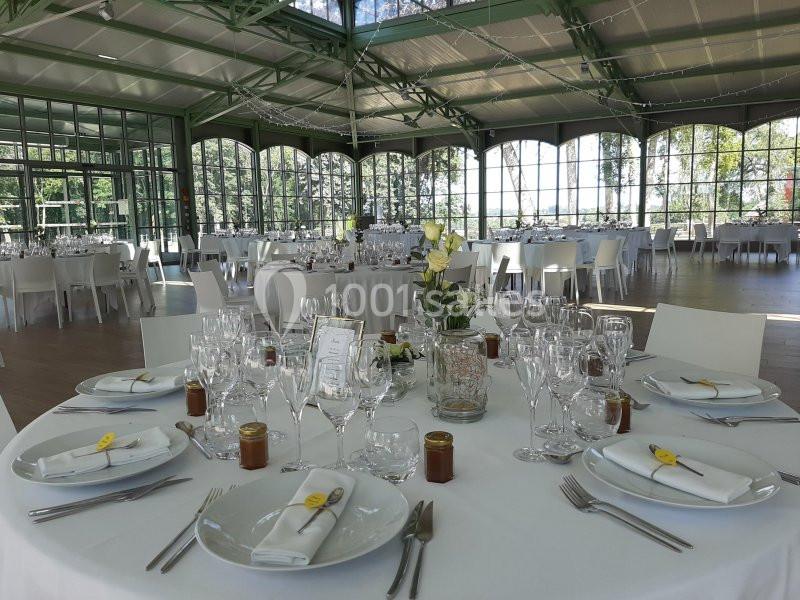 Salle de réception lumineuse avec tables rondes élégamment dressées, décorée de fleurs et de verrerie raffinée.