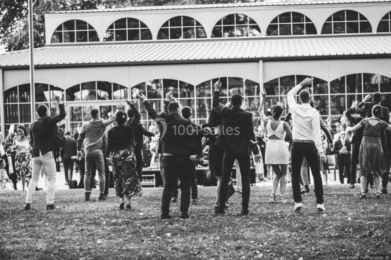 Groupe de personnes dansant en extérieur devant un bâtiment avec de grandes fenêtres, ambiance festive.
