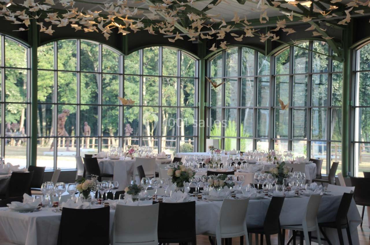 Salle de réception lumineuse avec de grandes baies vitrées, tables dressées et décorations en forme d'oiseaux suspendus.