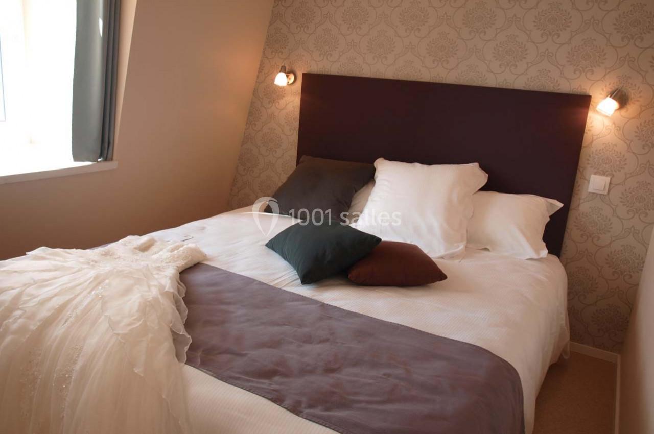 Lit double avec une couverture blanche, des coussins colorés et une robe de mariée posée sur le côté.