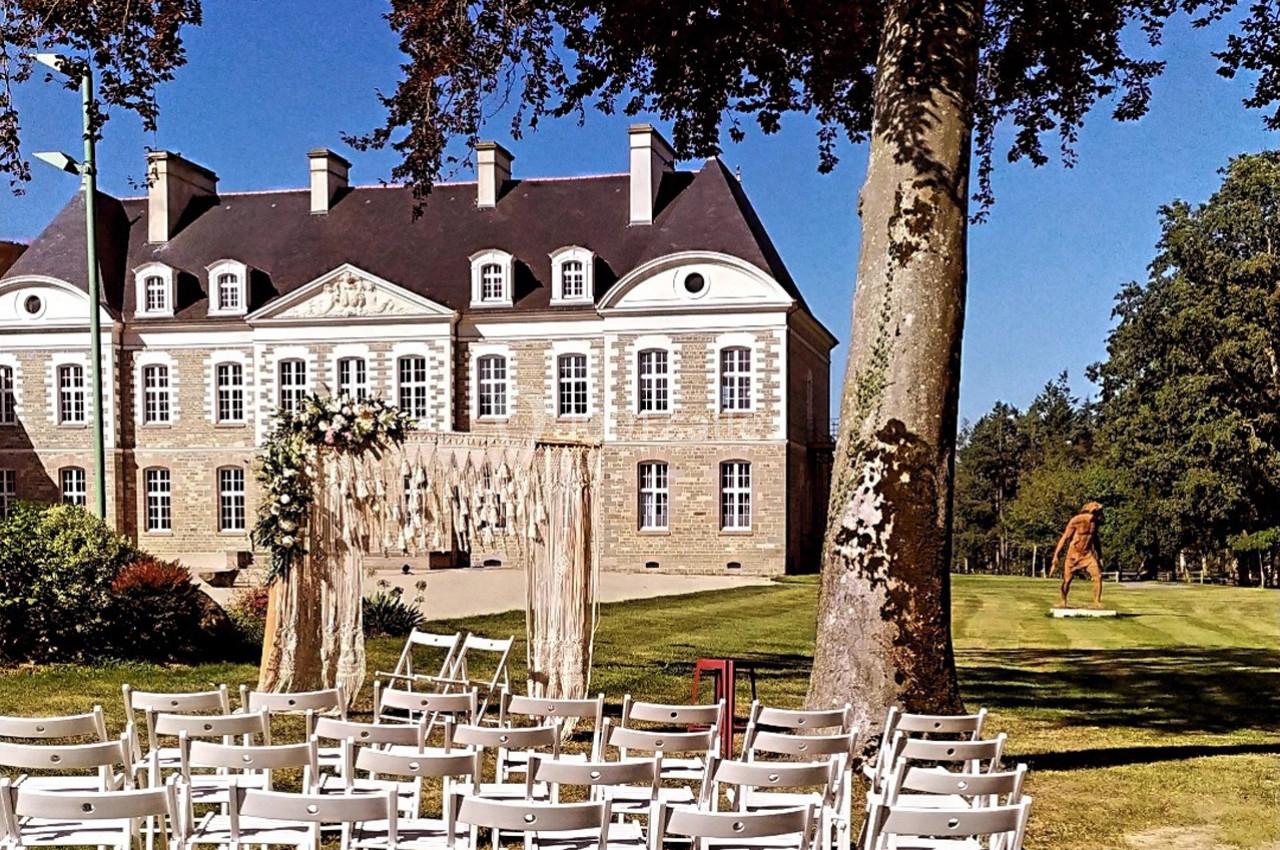 Chaises blanches disposées en plein air devant une arche décorée, avec un château en arrière-plan sous un ciel bleu.