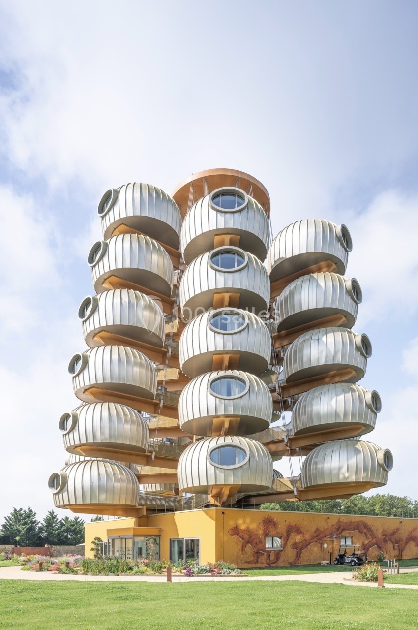 Immeuble moderne avec des balcons arrondis en forme de capsules métalliques, entouré de pelouse et d'arbres.
