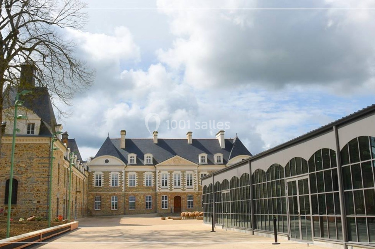 Façade d'un château ancien en pierre avec une extension moderne vitrée sous un ciel partiellement nuageux.