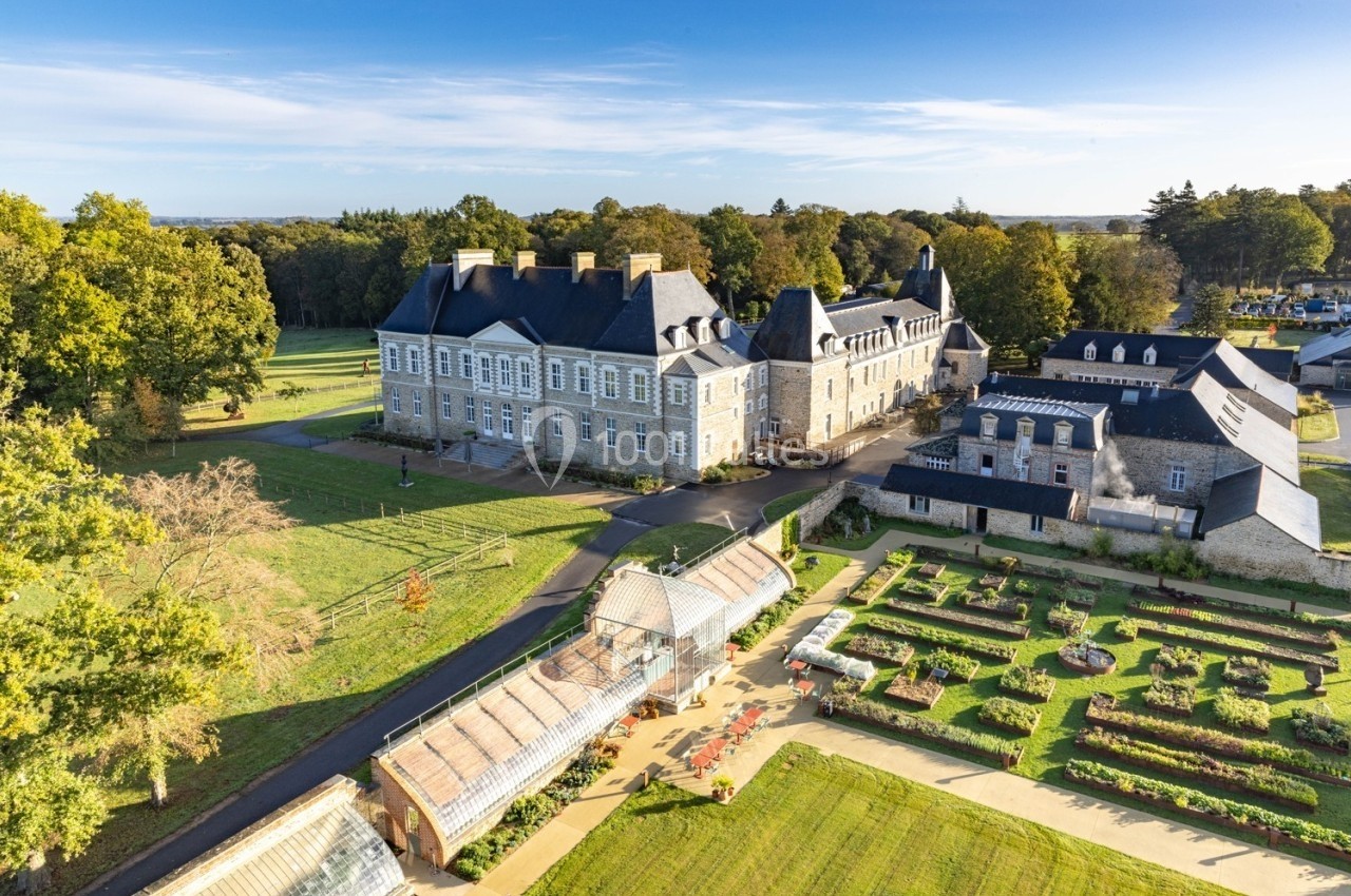 Vue aérienne d'un château entouré de jardins aménagés, de serres et d'espaces verts arborés.