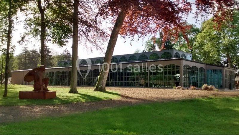 Serre moderne entourée d'arbres, avec une statue en métal au premier plan sur une pelouse.