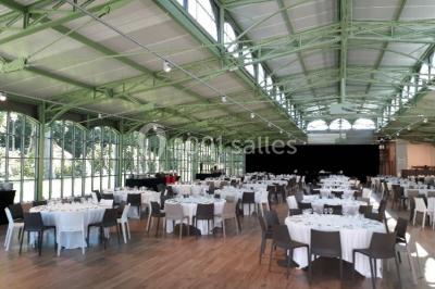 Salle de restaurant chaleureuse avec tables en bois, chaises en rotin, rideaux rouges et éclairage suspendu.