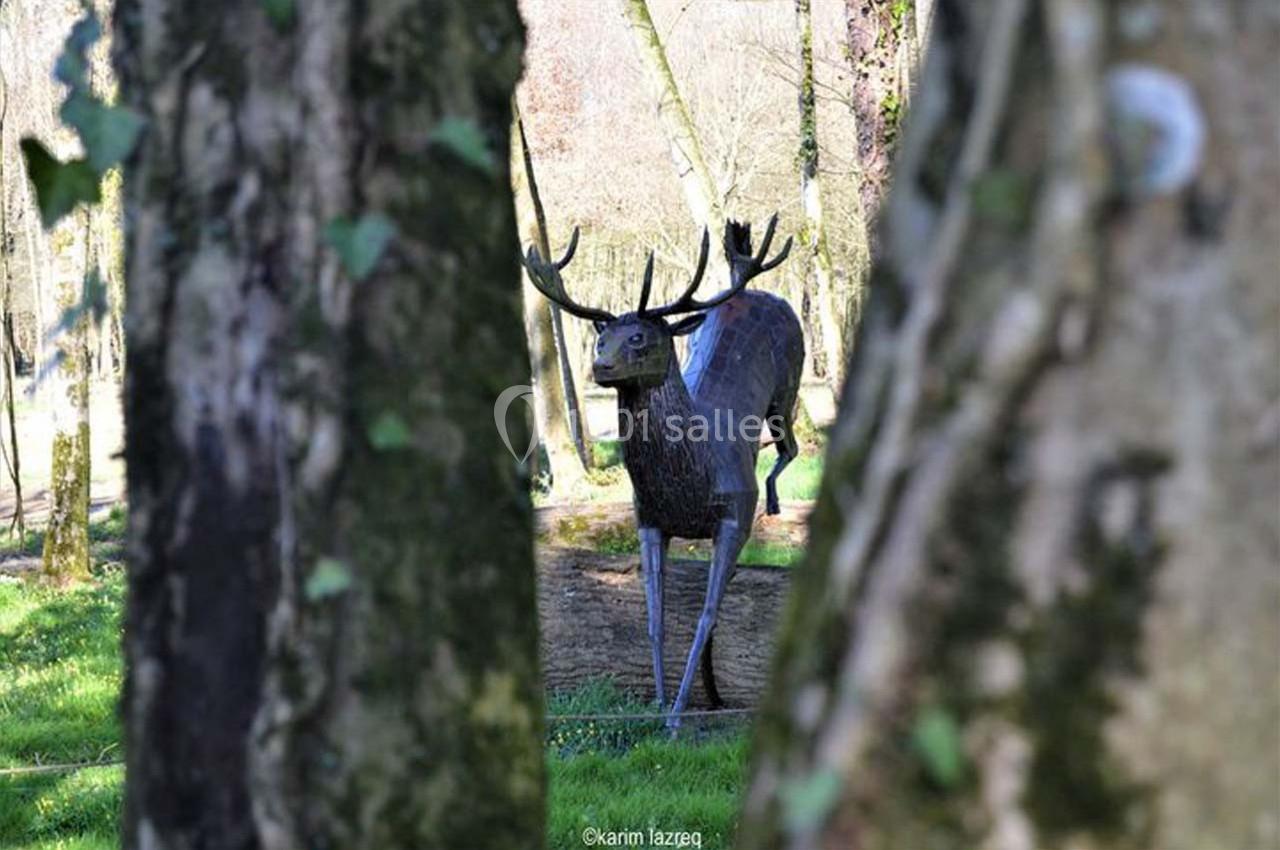 Statue d'un cerf en métal vue à travers les troncs d'arbres dans un parc verdoyant.