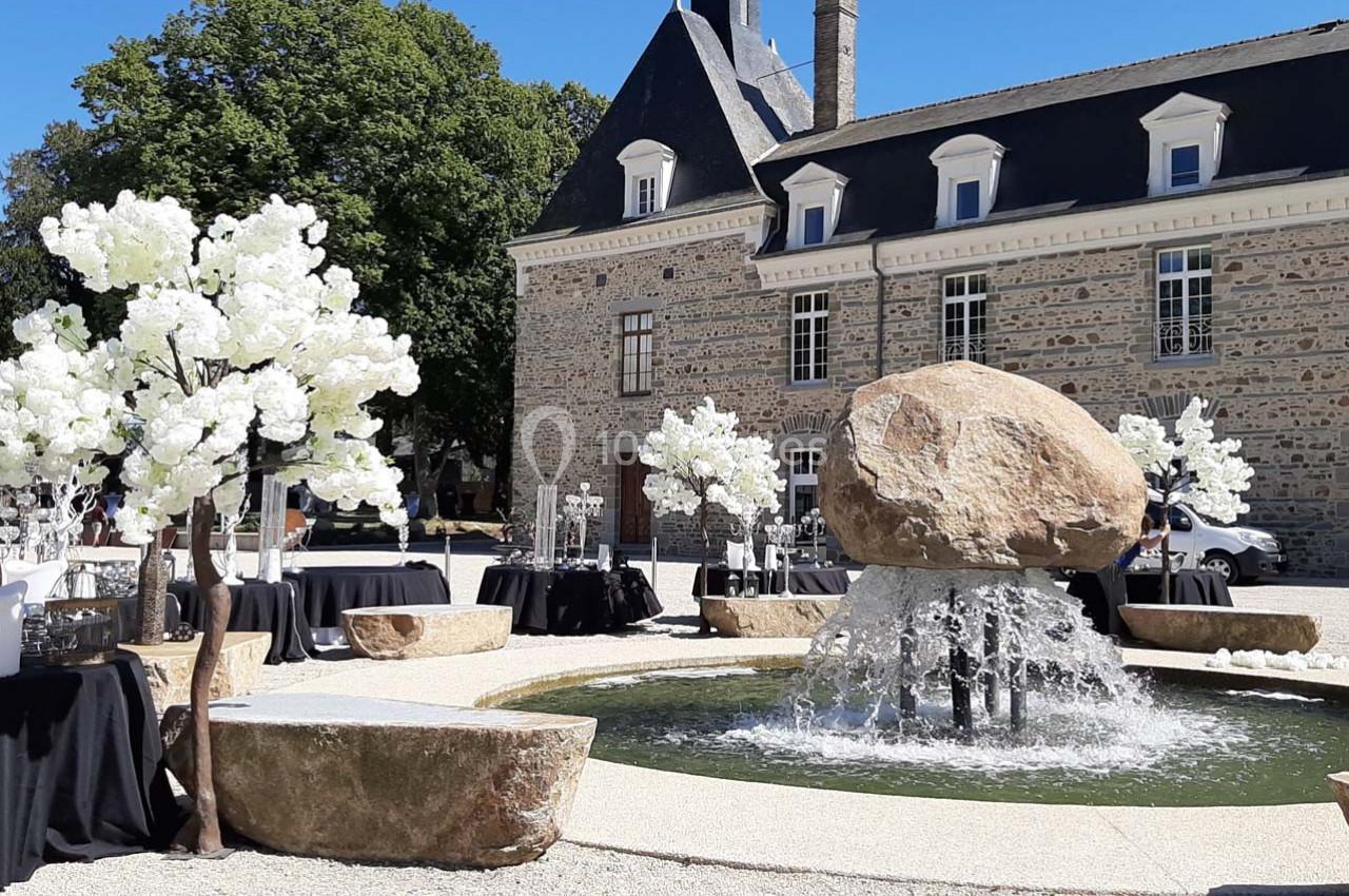Fontaine entourée de tables décorées et d'arbres artificiels blancs devant un bâtiment en pierre historique.