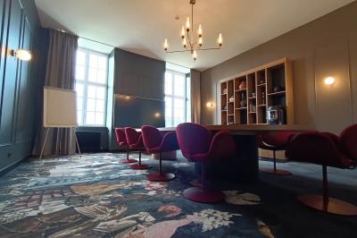 Salle de restaurant chaleureuse avec tables en bois, chaises en rotin, rideaux rouges et éclairage suspendu.
