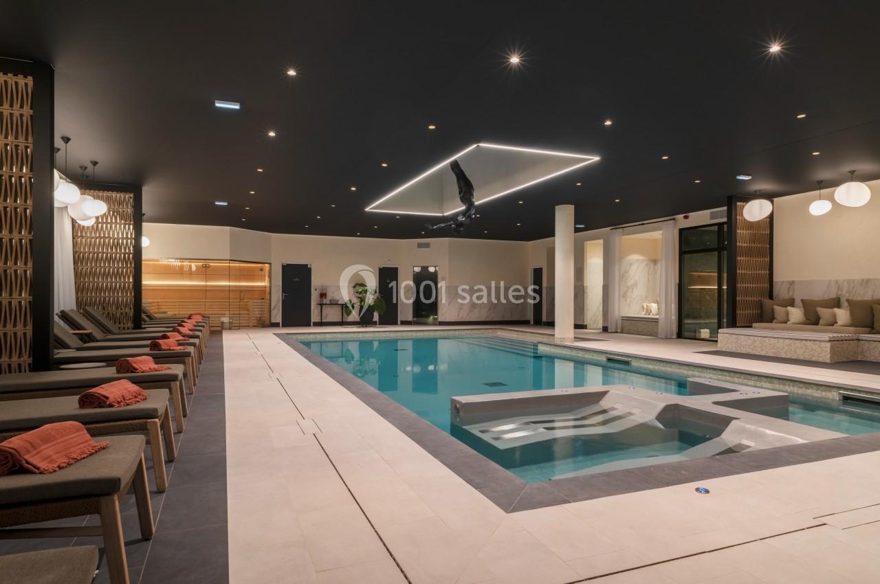 Piscine intérieure moderne entourée de chaises longues avec serviettes, éclairage tamisé et décor élégant.