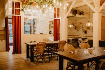 Salle de restaurant chaleureuse avec tables en bois, chaises en rotin, rideaux rouges et éclairage suspendu.