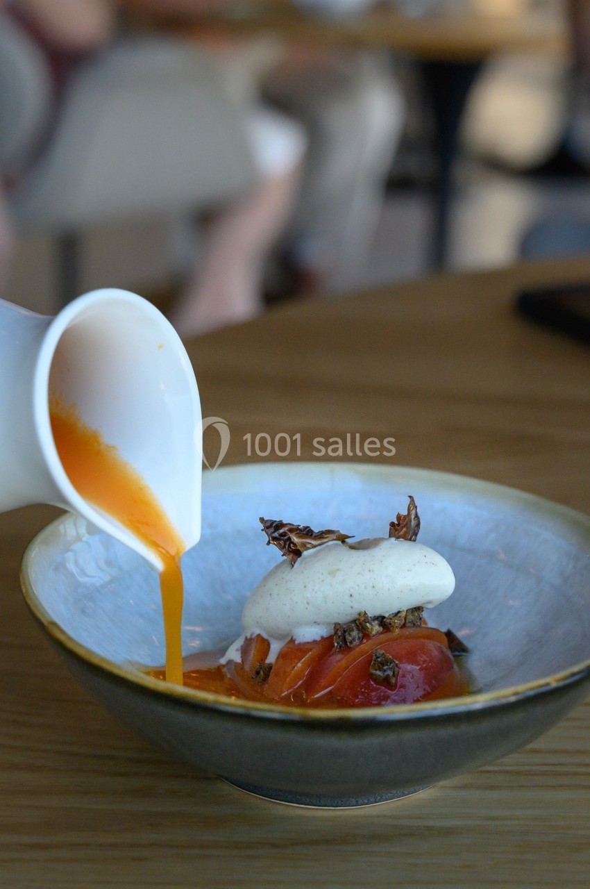 Un coulis orange est versé sur un plat composé de tomates, mousse blanche et garnitures croustillantes.