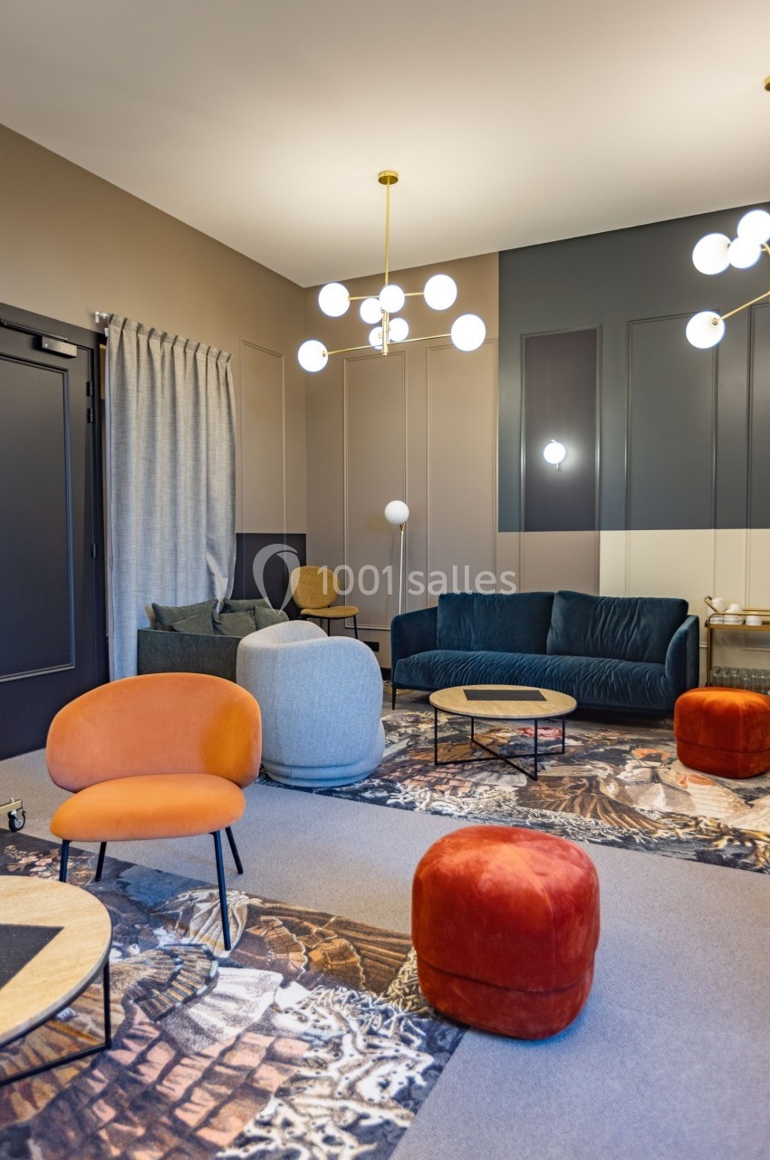 Salon moderne avec fauteuils colorés, canapé vert, tables basses en bois et luminaires suspendus dans un décor chaleureux.