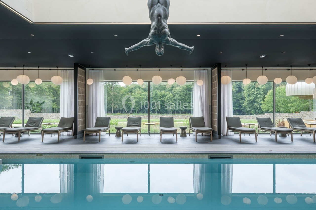 Un bassin intérieur avec des chaises longues alignées devant de grandes baies vitrées donnant sur un jardin.