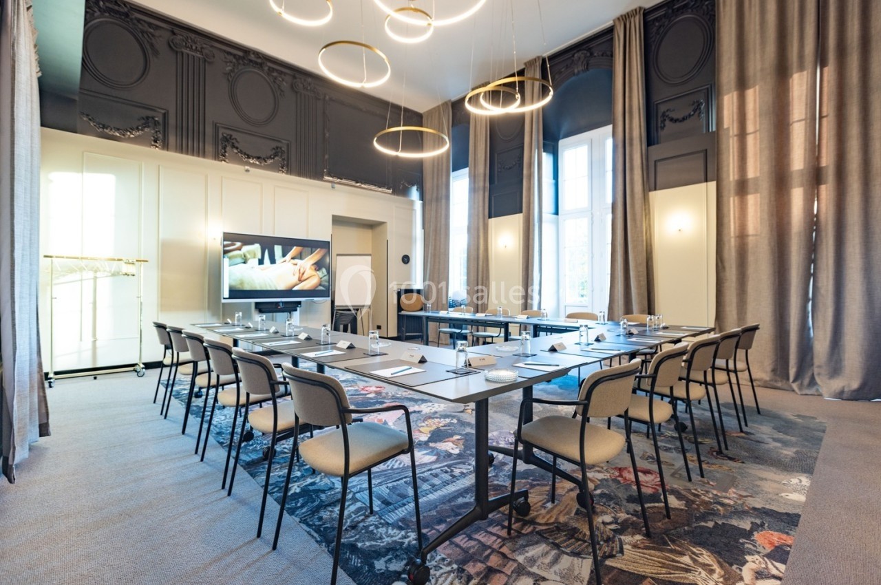 Salle de réunion lumineuse avec une grande table rectangulaire, chaises, écran de présentation et rideaux élégants.