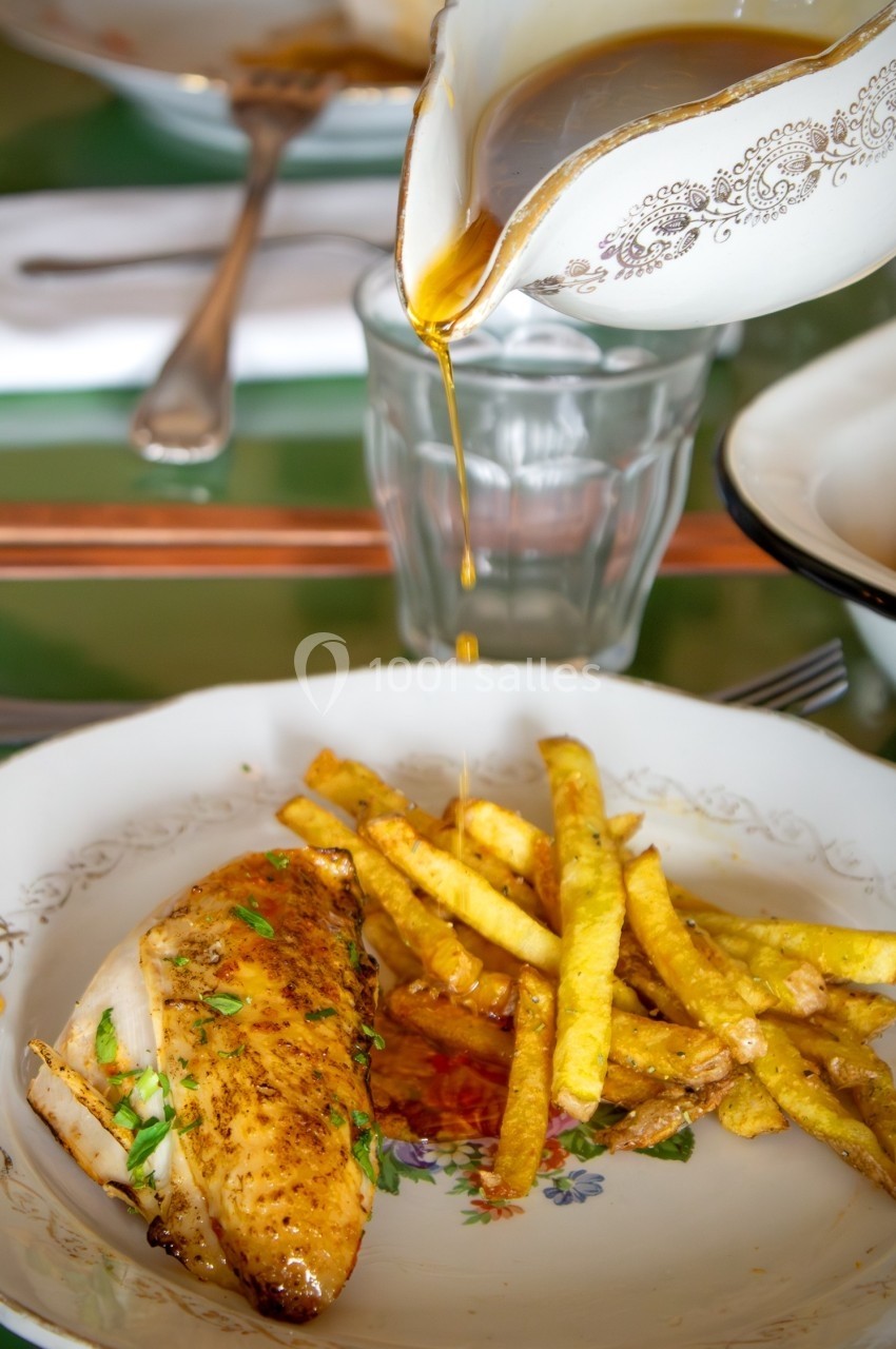 Poulet rôti avec des frites dorées, nappé de sauce versée depuis une saucière décorée.
