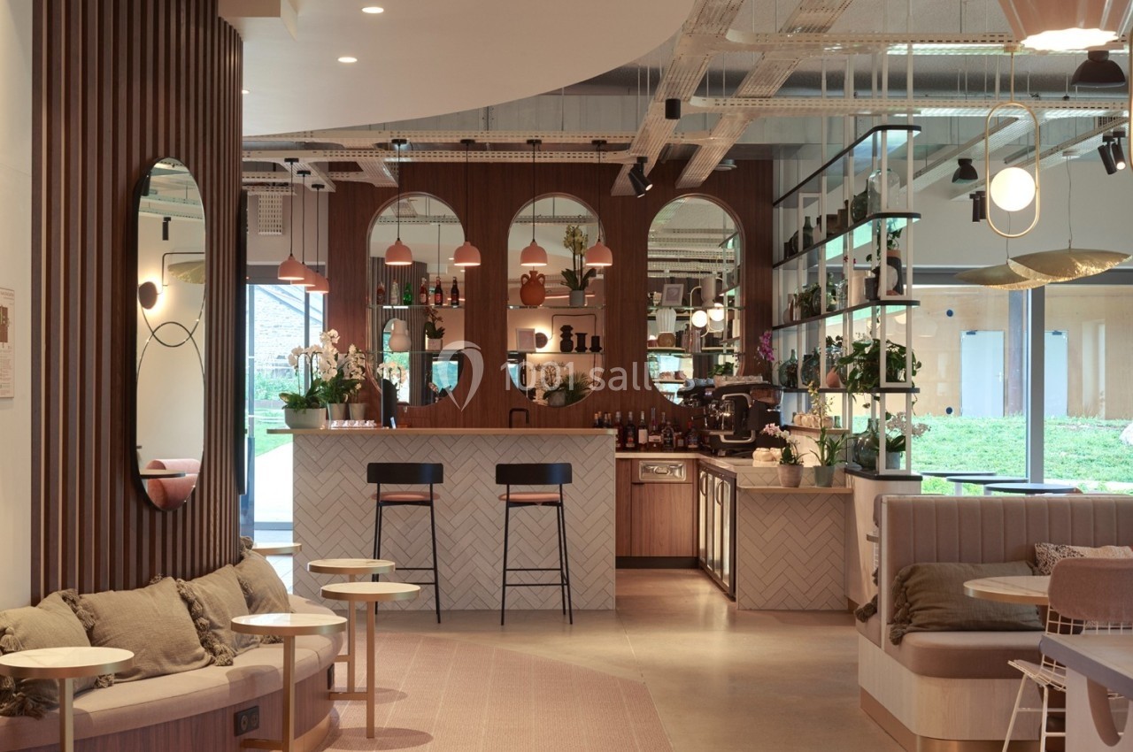 Espace intérieur moderne avec un bar central, des tables, des miroirs et une décoration chaleureuse en bois et tons neutres.