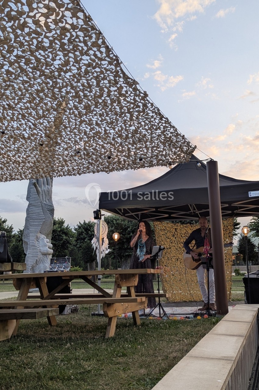 Deux musiciens jouent sous un chapiteau en plein air près de tables de pique-nique, au coucher du soleil.