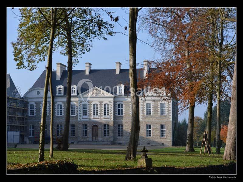 Façade d'un manoir en pierre entouré d'arbres, sous un ciel clair et ensoleillé.