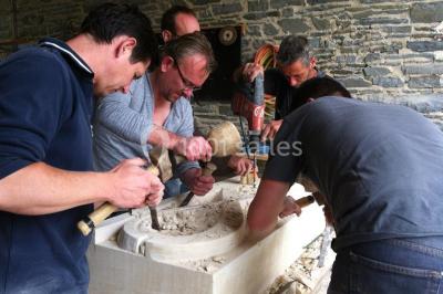 Salle de restaurant chaleureuse avec tables en bois, chaises en rotin, rideaux rouges et éclairage suspendu.
