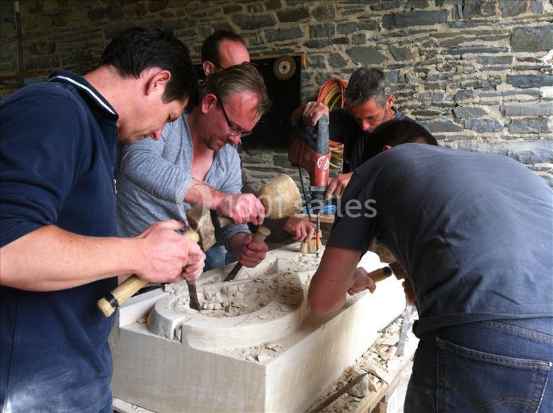 Des artisans sculptent un bloc de pierre à l'aide de maillets et de ciseaux dans un atelier en pierre.