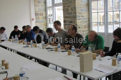 Salle de restaurant chaleureuse avec tables en bois, chaises en rotin, rideaux rouges et éclairage suspendu.