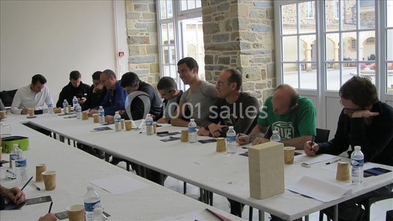 Des personnes assises autour d'une table en réunion, prenant des notes dans une salle lumineuse avec des fenêtres.