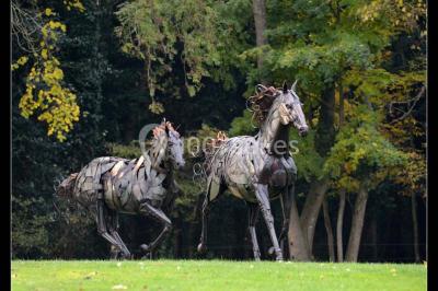 Salle de restaurant chaleureuse avec tables en bois, chaises en rotin, rideaux rouges et éclairage suspendu.
