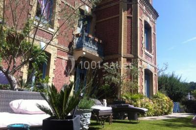 Décor champêtre avec fauteuils, tapis, grande horloge et lanternes sous un arbre, ambiance vintage en extérieur.