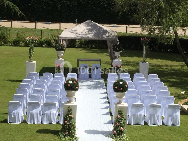 Allée centrale décorée de fleurs menant à une arche de cérémonie en plein air, entourée de chaises blanches.