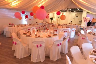 Décor champêtre avec fauteuils, tapis, grande horloge et lanternes sous un arbre, ambiance vintage en extérieur.