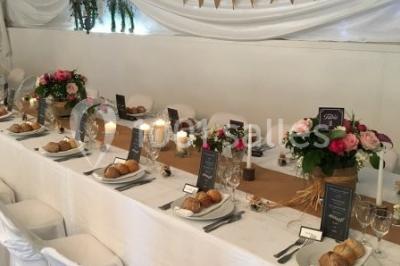 Décor champêtre avec fauteuils, tapis, grande horloge et lanternes sous un arbre, ambiance vintage en extérieur.